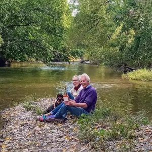 Richard and Diana sat next to the river bank with their dogs.